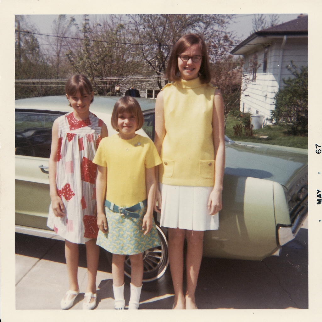 Cheryl--the proud Mustang owner--should be *in* this picture. But she was the one *taking* this terrific Polaroid instead. That's my sister Bev, me in the middle, and my sister Marilee hiding the automotive icon.