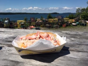 Photo of lobster roll on picnic table next to bay.