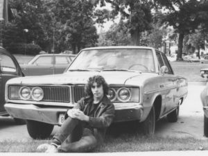 Photo of the author in a black leather jacket, sitting on the ground in front of his Dodge Dart.